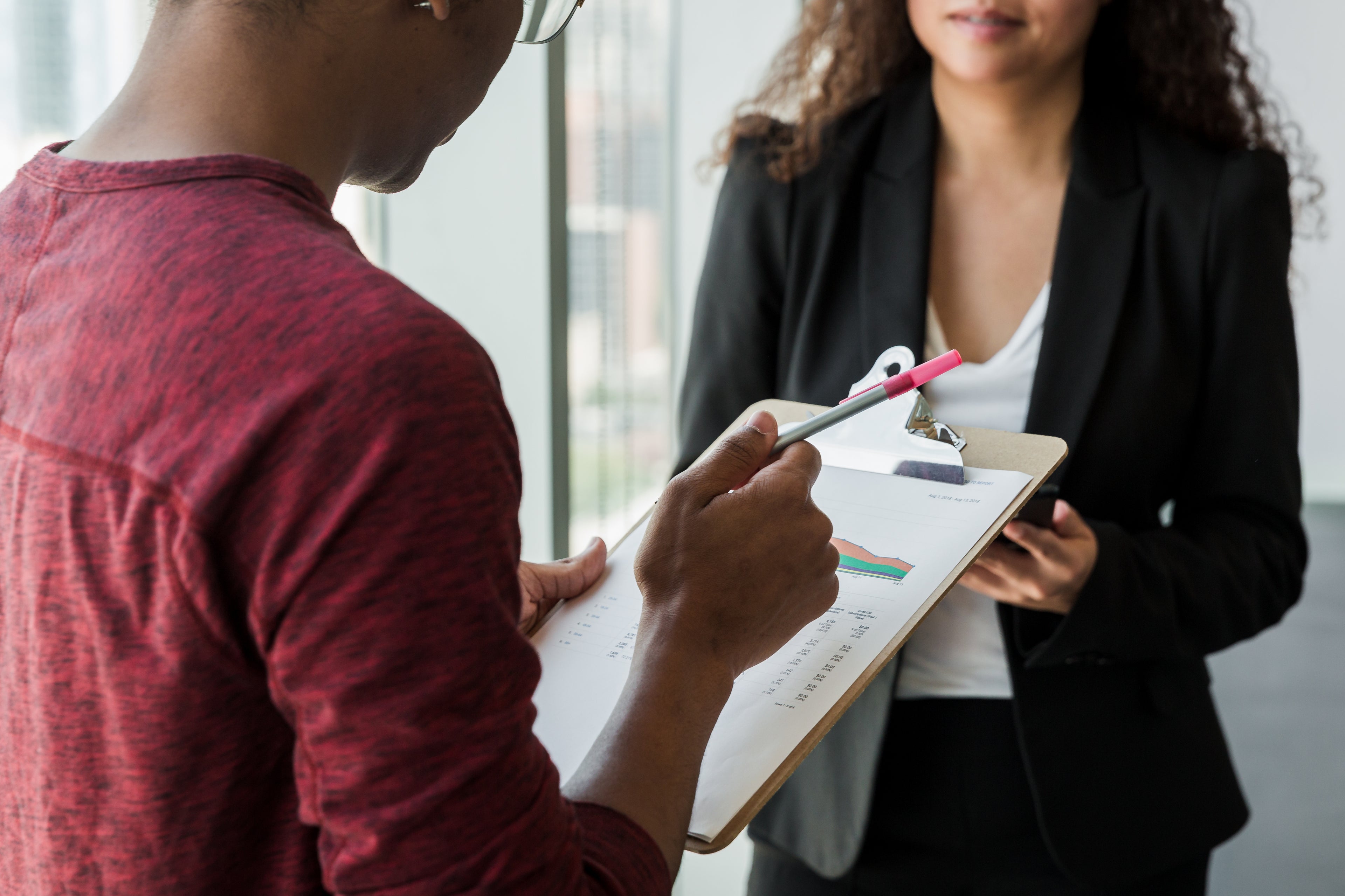 man holding clipboard while talking to a woman in an office setting