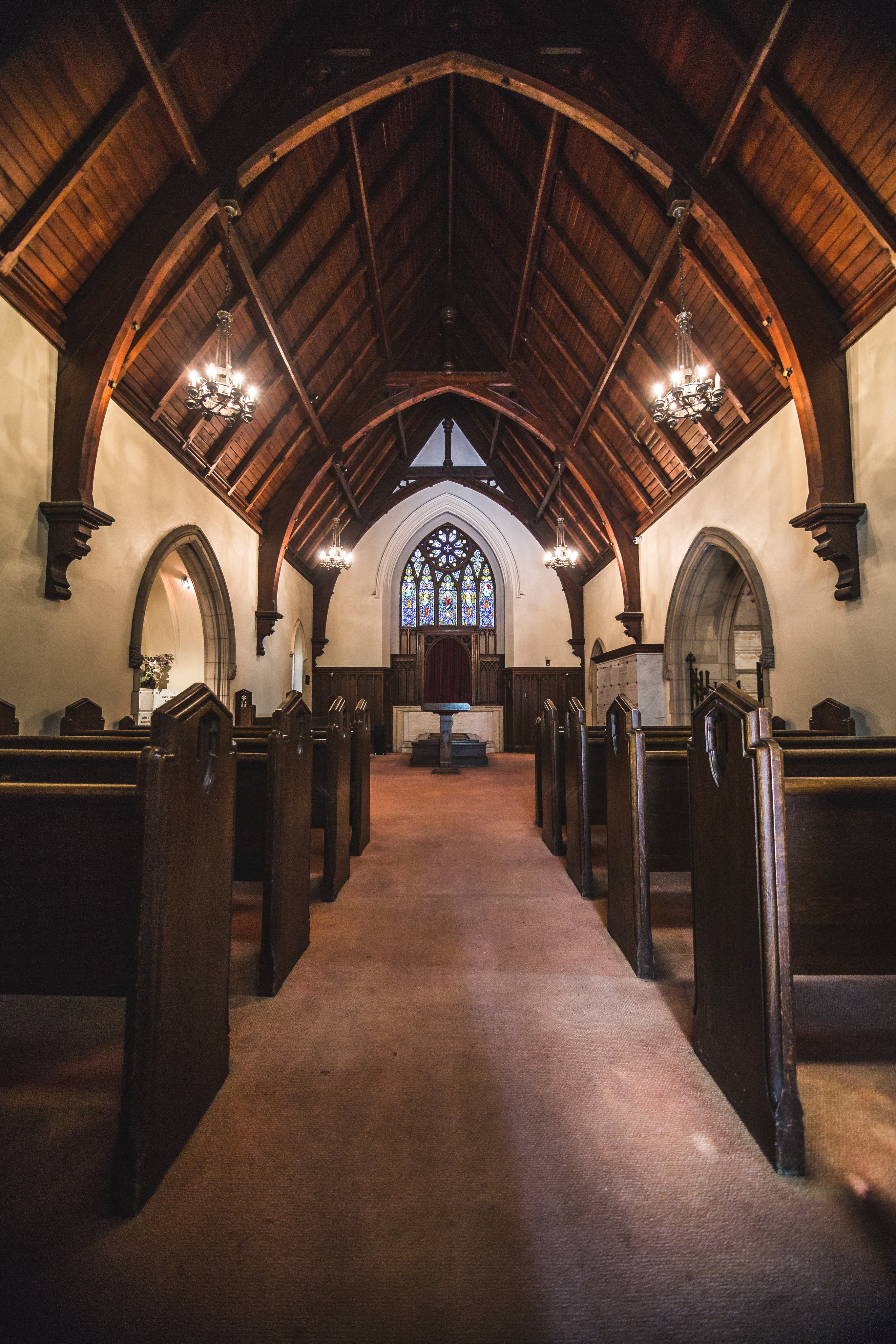 small chapel interior with pews lights and stained glass window